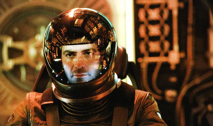 George Clooney wears a white space suite inside a spaceship with orange lighting